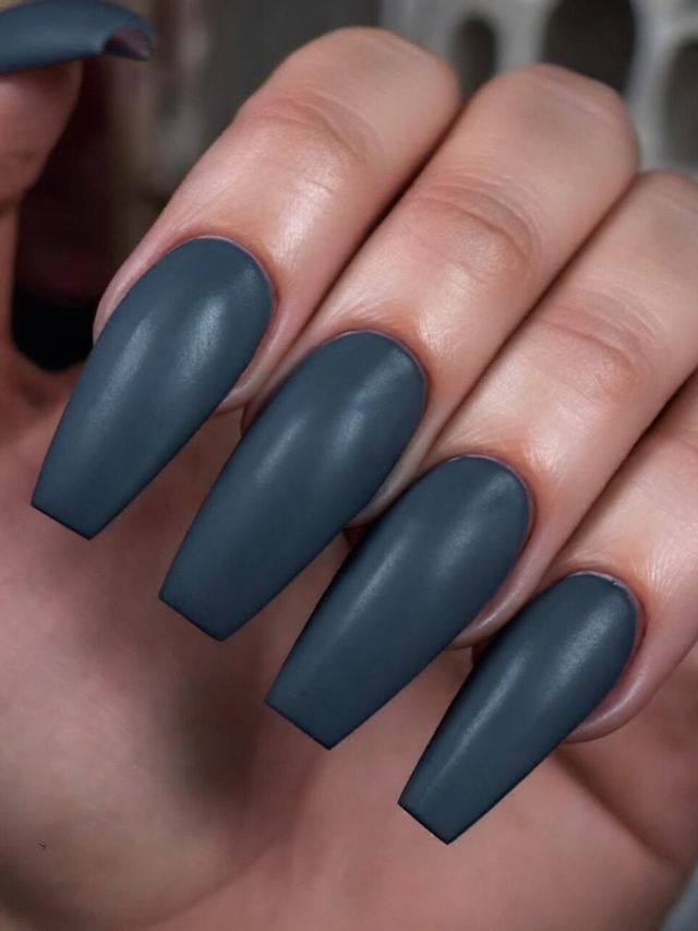 A woman's hand holding a pair of dark grey nails.