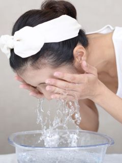 A woman is washing her face with water from a bowl.