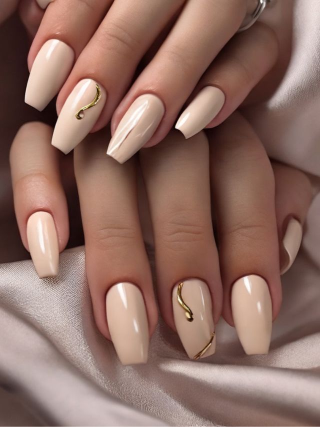 A woman's hands with beige nails and gold accents.