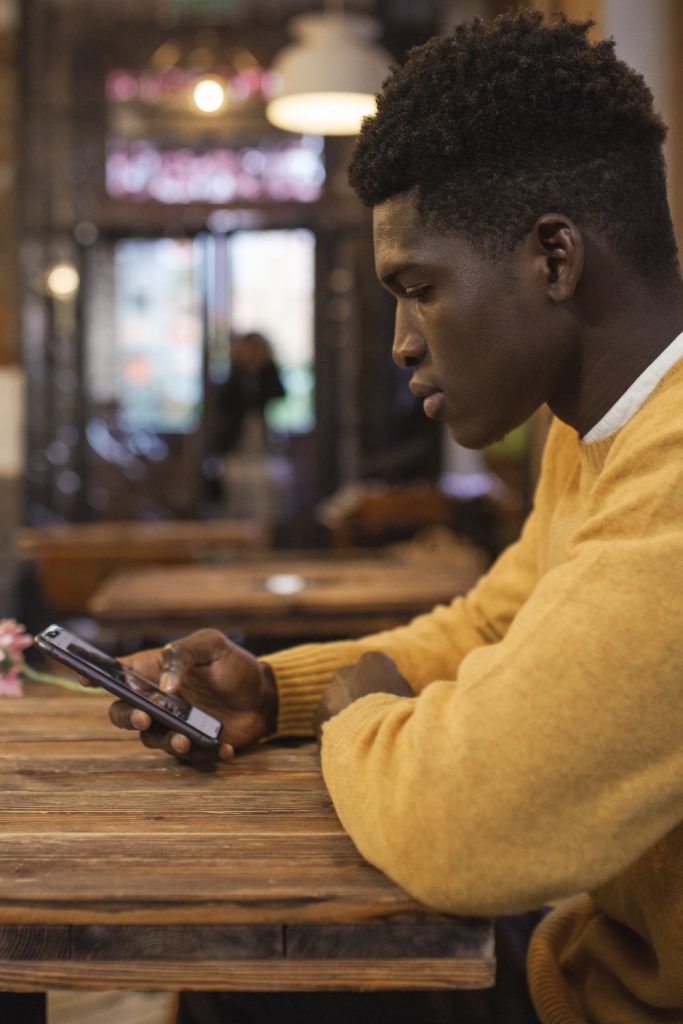 A young black man using his cell phone in a cafe