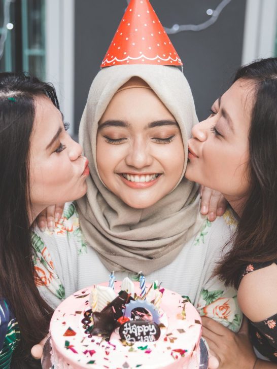 Three Muslim women lovingly kiss a birthday cake as a gesture of gratitude for the gifts received.