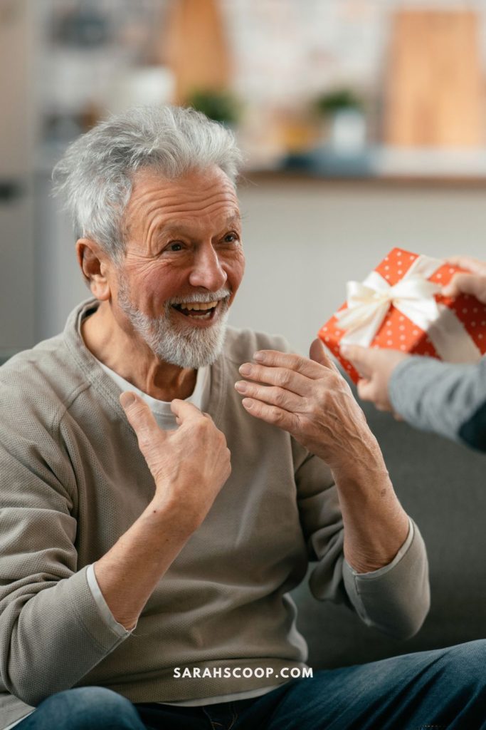 Elderly man with a cheerful expression receives a gift from someone off-camera.